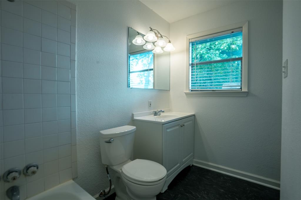 1285 Clark Road Gainesville, TX 76240 - Photo 5 of 20 Bathroom featuring a white vanity with an integrated sink, a mirror with an overhead light fixture, a window with blinds, and tiled walls surrounding the bathtub