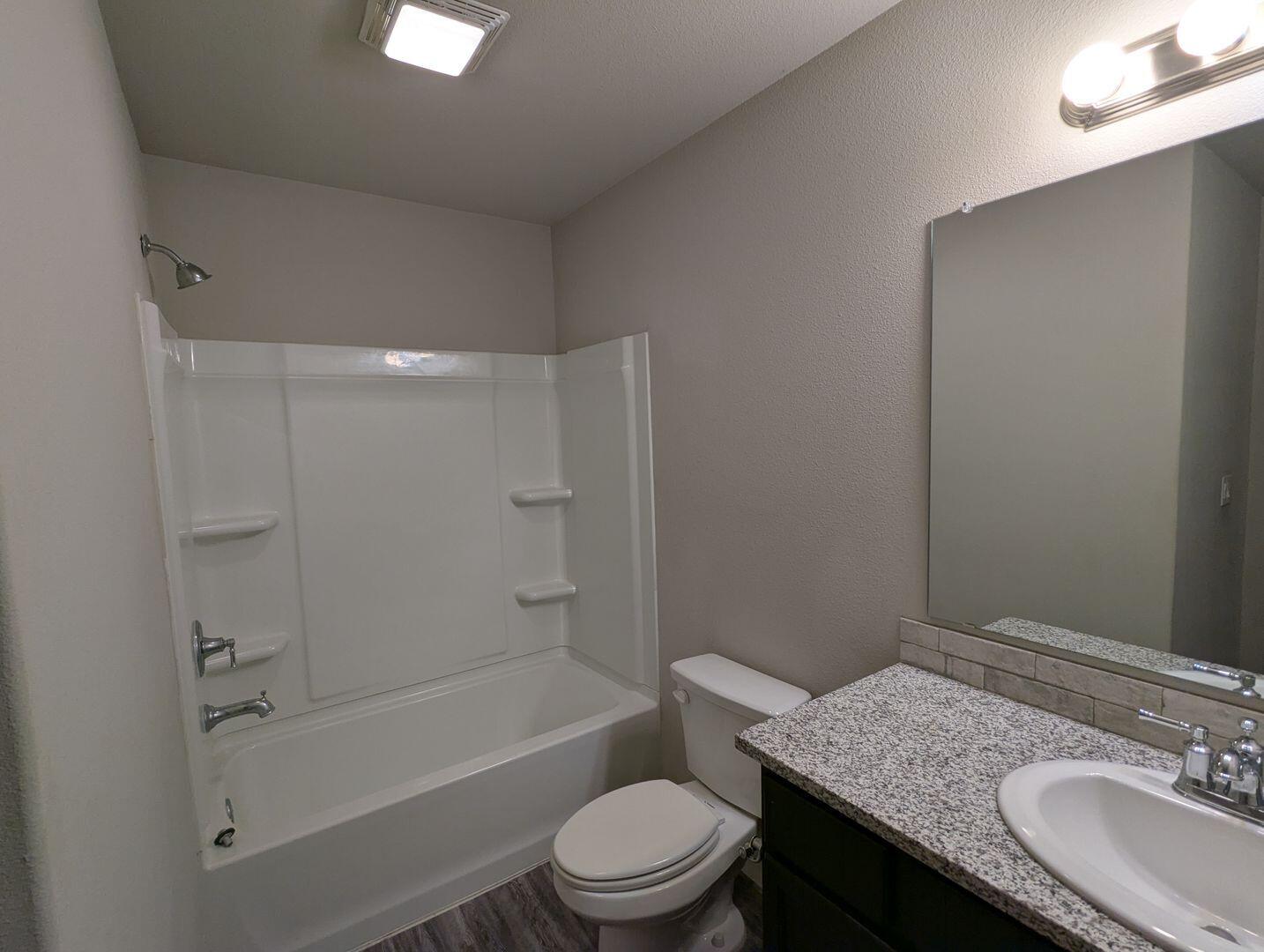 1628 133rd Street, Unit A Lubbock, TX 79423 - Photo 11 of 11 a bathroom with a granite countertop sink toilet a mirror and shower