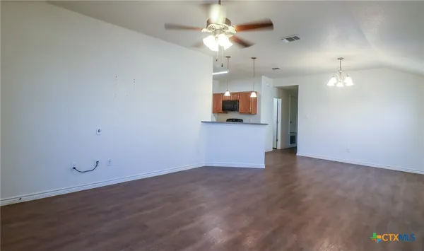 an empty room with wooden floor chandelier and windows