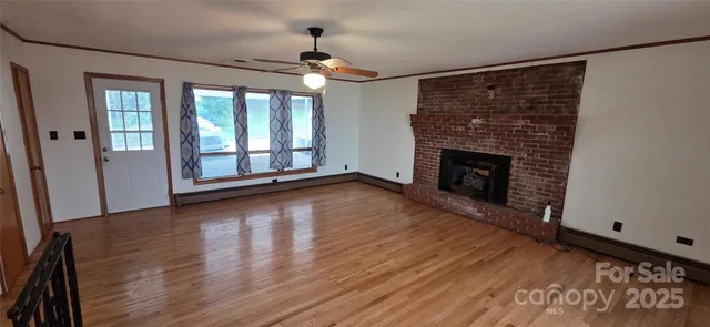 a view of an empty room with wooden floor fireplace and a window