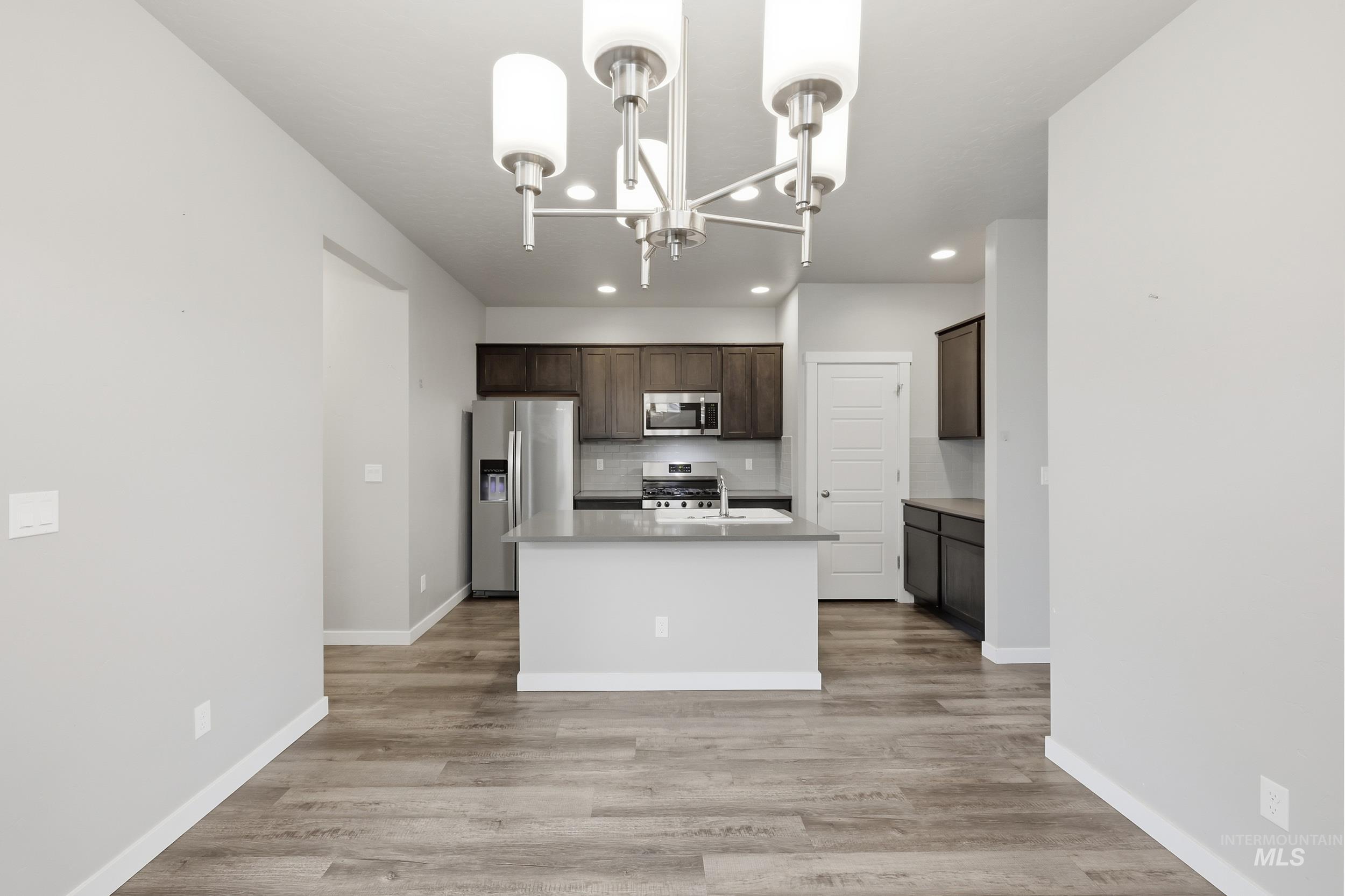 1097 North World Cup Lane Eagle, ID 83616 - Photo 10 of 42 Kitchen featuring stainless steel appliances, dark wood finish cabinetry, a kitchen island with sink, light wood-style floors, and hanging lights