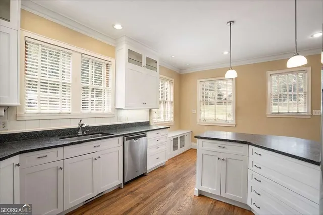 a kitchen with granite countertop white cabinets white appliances wooden floor and a window