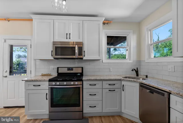 a kitchen with granite countertop white cabinets appliances a window and a sink