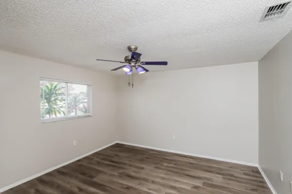a view of an empty room with wooden floor and a fan