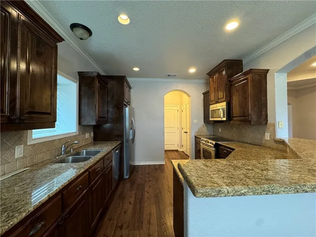 a kitchen with granite countertop stainless steel appliances a sink stove top oven and cabinets
