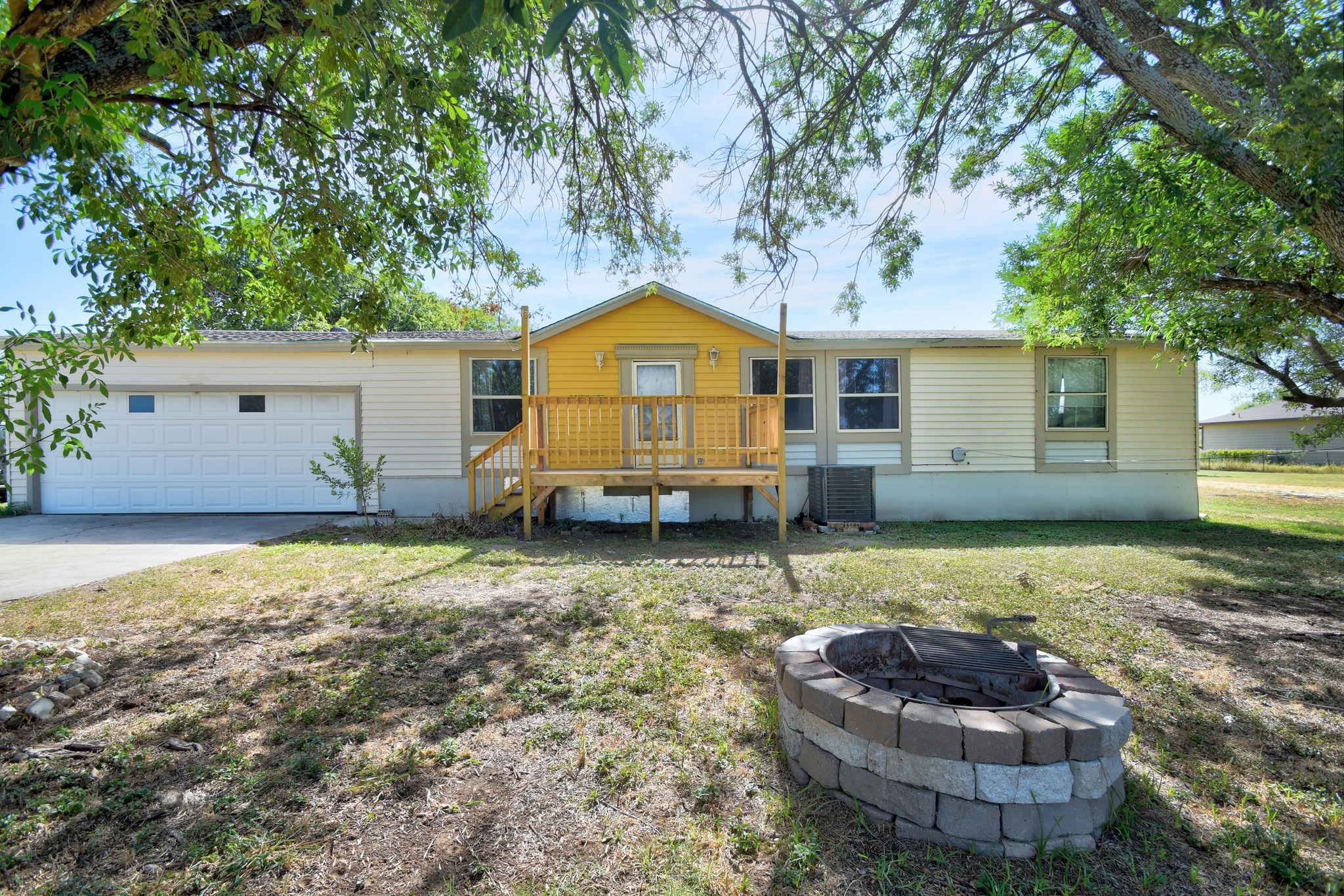 17398 Benton City Road Von Ormy, TX 78073 - Photo 1 of 1 Back of house with a deck, an attached garage, driveway, a fire pit, and a lawn