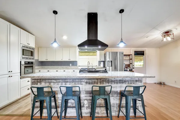 a kitchen with stainless steel appliances granite countertop a dining table chairs and white cabinets