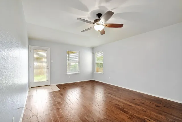 an empty room with wooden floor fan and windows