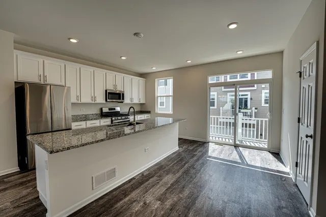 a kitchen with granite countertop a refrigerator a sink a stove a microwave and island with wooden floor