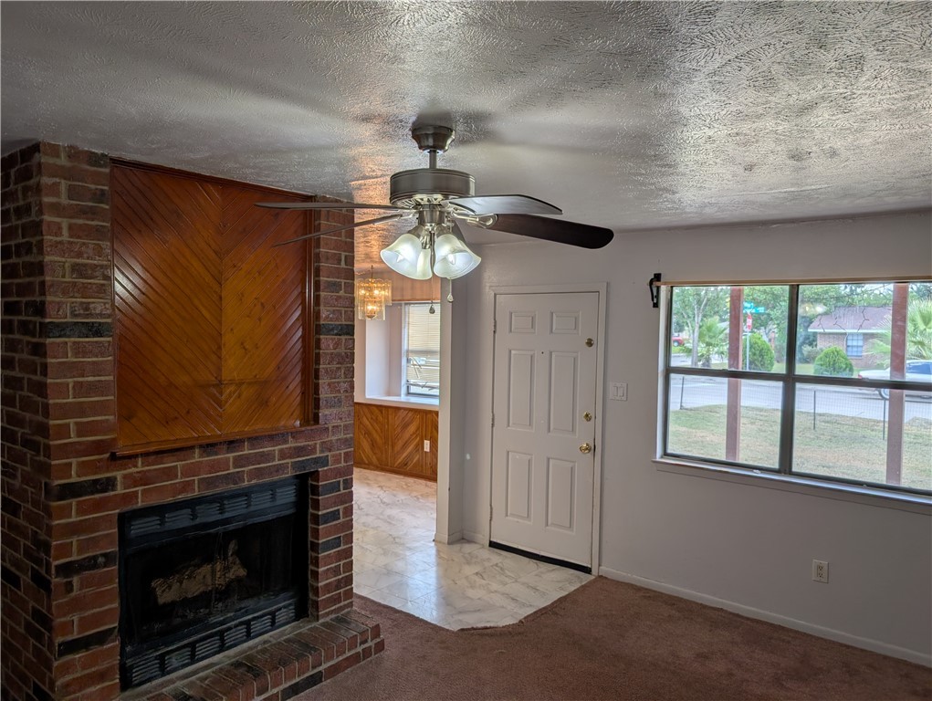 2901 Minnesota Avenue Bryan, TX 77803 - Photo 4 of 16 Unfurnished living room featuring carpet flooring, wooden walls, a brick fireplace, a textured ceiling, and a ceiling fan