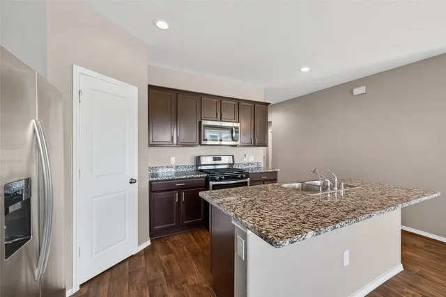 a view of a kitchen with kitchen island a sink wooden floor and stainless steel appliances