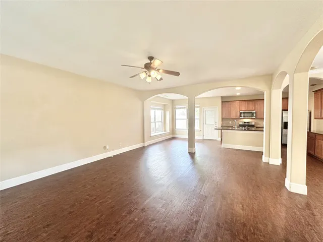 a view of an empty room with wooden floor and a kitchen