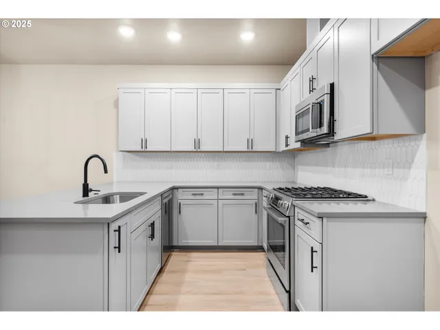 a kitchen with stainless steel appliances granite countertop a sink a stove a refrigerator a white cabinet with grey and white cabinets