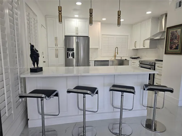 a kitchen with stainless steel appliances kitchen island granite countertop a table chairs refrigerator and microwave
