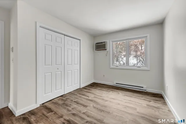 an empty room with wooden floor closet and windows