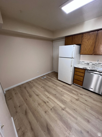 556 North Fairfield Road, Unit D4 Layton, UT 84041 - Photo 2 of 23 Kitchen with stainless steel dishwasher, brown cabinets, freestanding refrigerator, light wood-style flooring, and light stone countertops