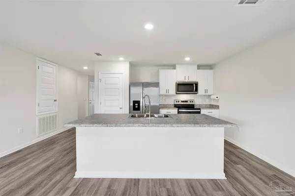 a large kitchen with stainless steel appliances granite countertop a stove a sink a refrigerator white cabinets and wooden floor