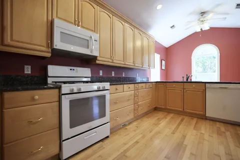 a kitchen with granite countertop a stove a sink and dishwasher wooden cabinets with granite countertops