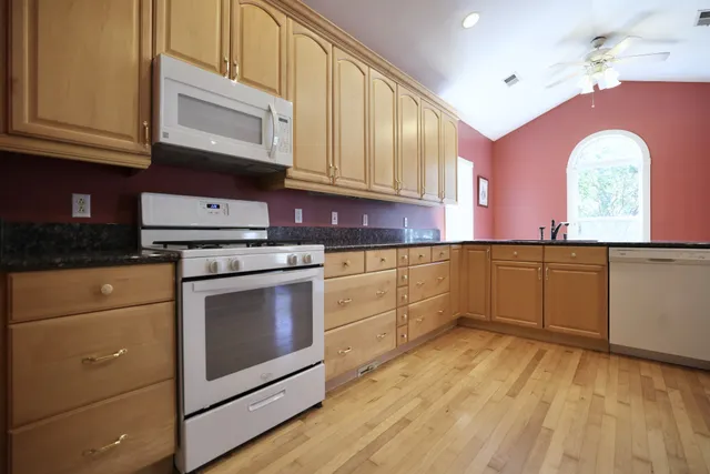 a kitchen with granite countertop a stove a sink and dishwasher wooden cabinets with granite countertops