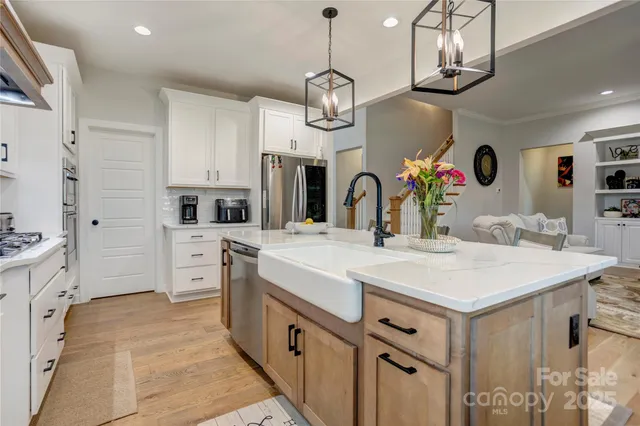 a kitchen with stainless steel appliances kitchen island granite countertop a stove a sink dishwasher and white cabinets with wooden floor