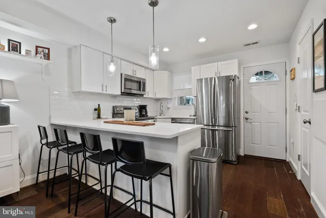 a kitchen with stainless steel appliances granite countertop a refrigerator a sink dishwasher a stove and white cabinets with wooden floor