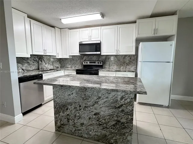a kitchen with granite countertop a refrigerator sink and white cabinets