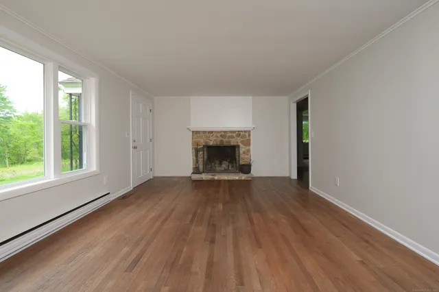 an empty room with wooden floor fireplace and windows