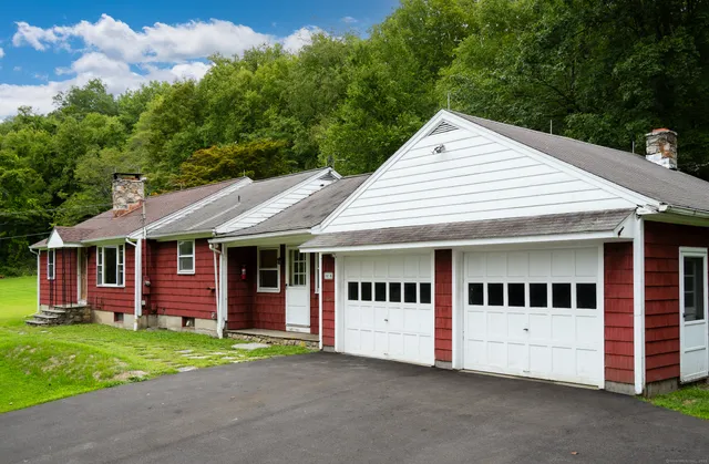 a view of a white house with a yard plants and large tree