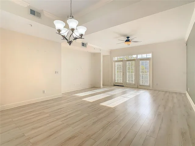 an empty room with wooden floor chandelier fan and windows