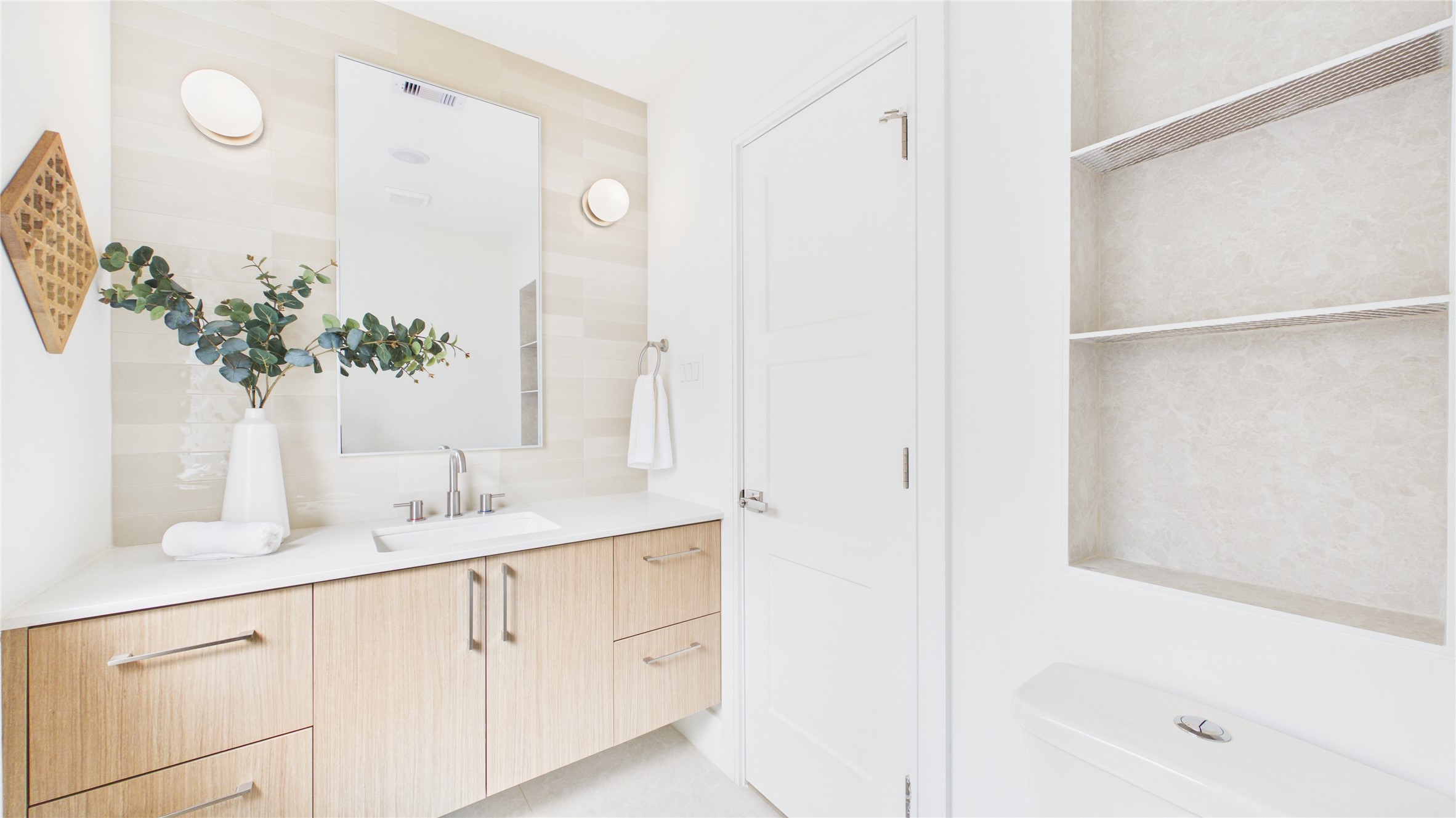 602 Skyland Terrace Way Houston, TX 77009 - Photo 12 of 40 This bathroom features a modern design with a light wood vanity, sleek countertop, and integrated sink. It includes a large mirror, wall-mounted lights, open shelving, and a contemporary toilet. The bright, neutral tones create a clean, airy feel.