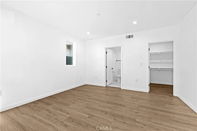 a view of an empty room with wooden floor closet and windows