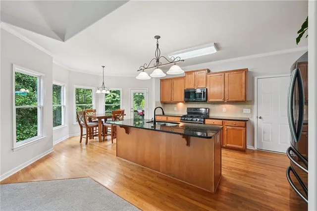 a kitchen with stainless steel appliances granite countertop a refrigerator a stove top oven a sink dishwasher a dining table and chairs with wooden floor
