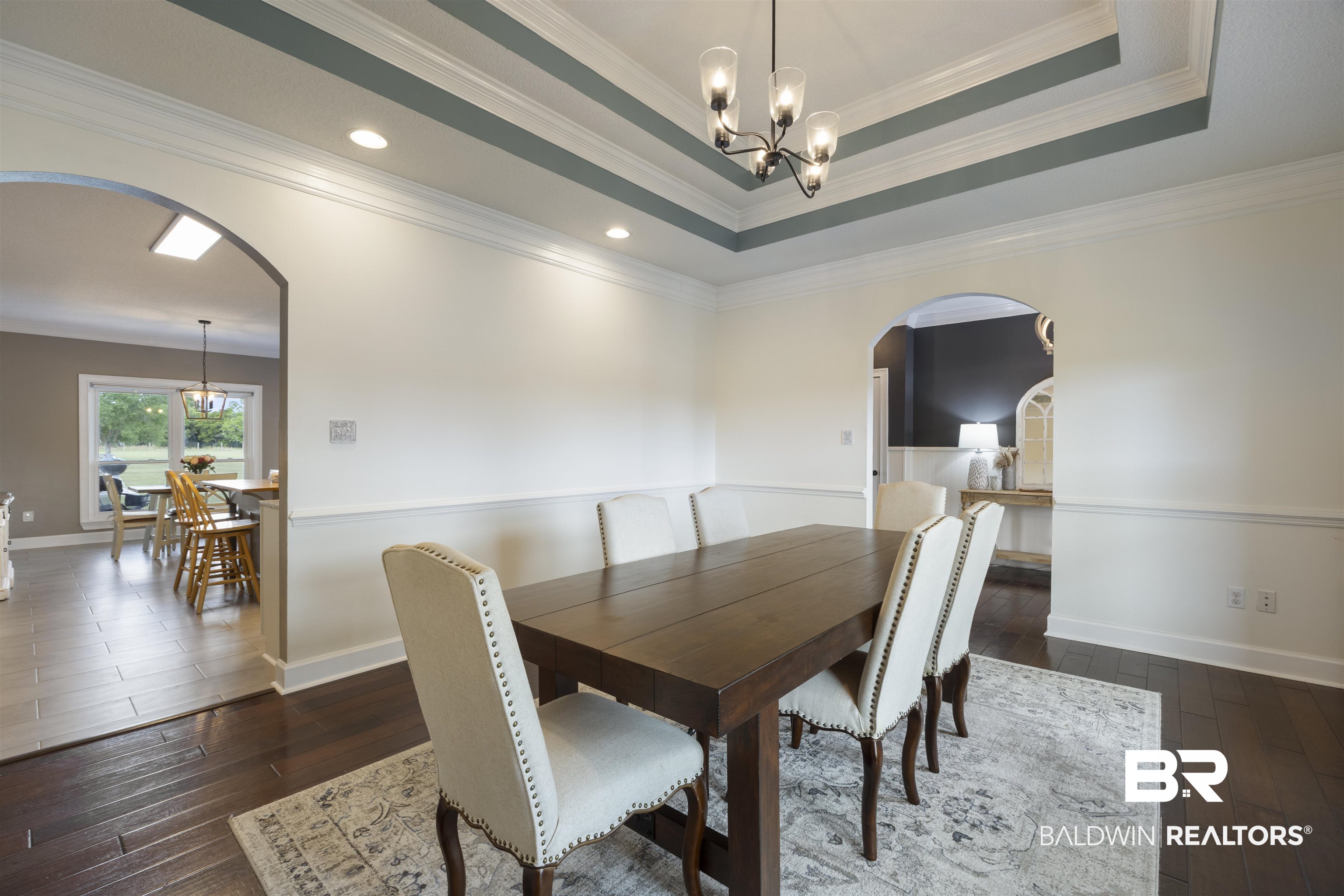 9855 Stucki Road Elberta, AL 36530 - Photo 13 of 54 Dining area with arched walkways, hanging lights, dark wood-style floors, crown molding, and a tray ceiling