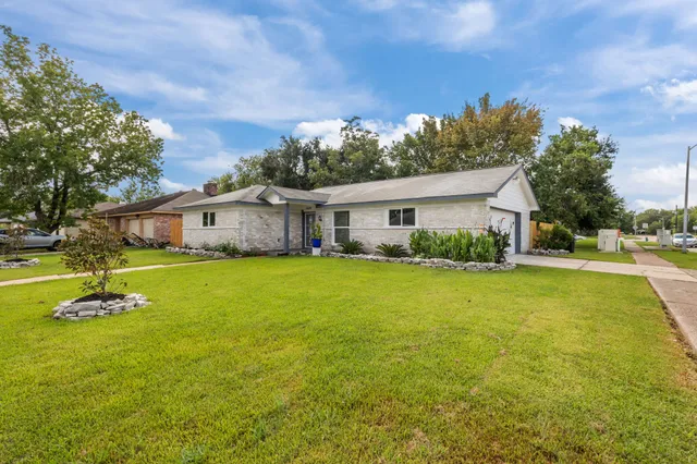 a white house with a big yard plants and large trees