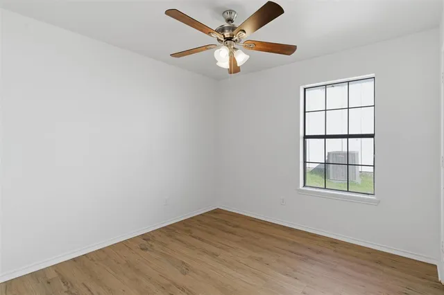 an empty room with wooden floor chandelier fan and windows