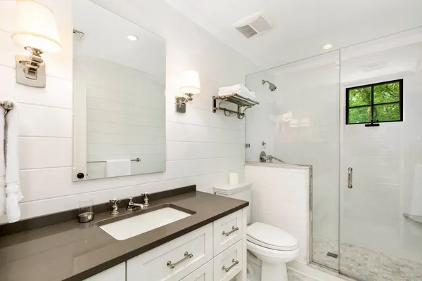 a bathroom with a granite countertop sink a toilet a mirror and shower