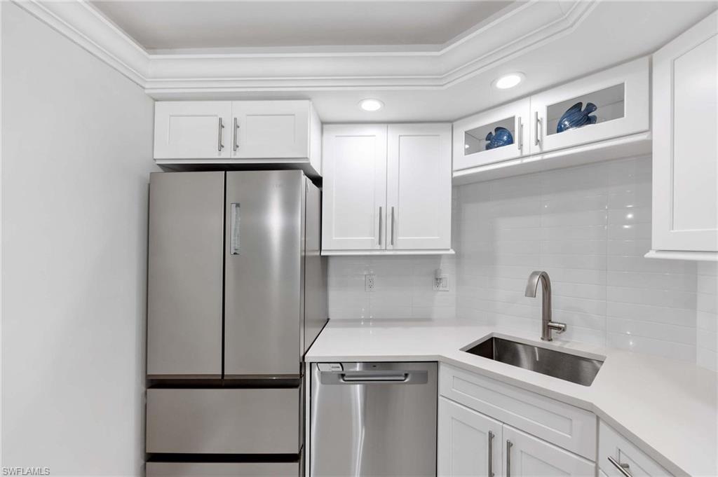 5 Bluebill Avenue, Unit 108 Naples, FL 34108 - Photo 4 of 49 Kitchen featuring stainless steel appliances, tasteful backsplash, white cabinetry, light countertops, and glass insert cabinets