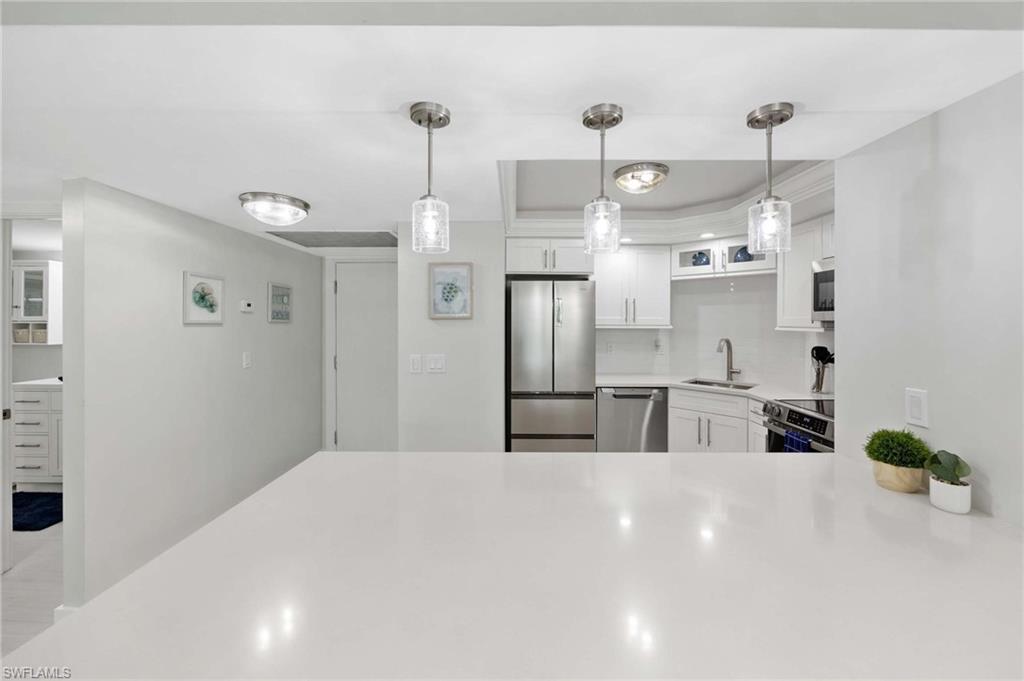 5 Bluebill Avenue, Unit 108 Naples, FL 34108 - Photo 5 of 49 Kitchen with stainless steel appliances, white cabinetry, light countertops, decorative backsplash, and pendant lighting