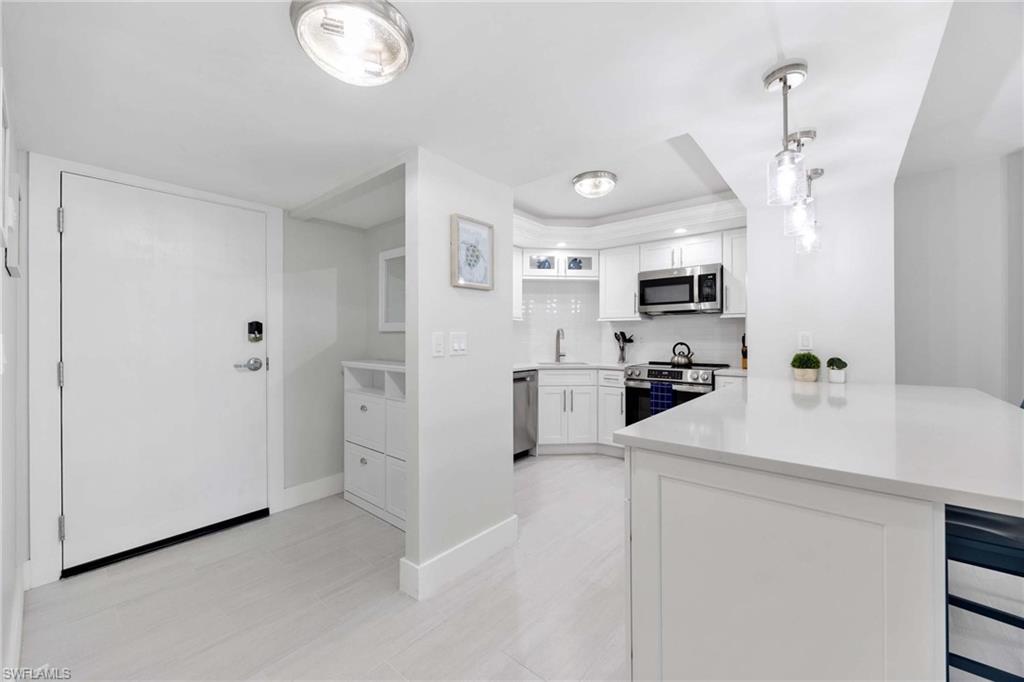 5 Bluebill Avenue, Unit 108 Naples, FL 34108 - Photo 6 of 49 Kitchen featuring appliances with stainless steel finishes, a peninsula, a tray ceiling, light countertops, and white cabinetry