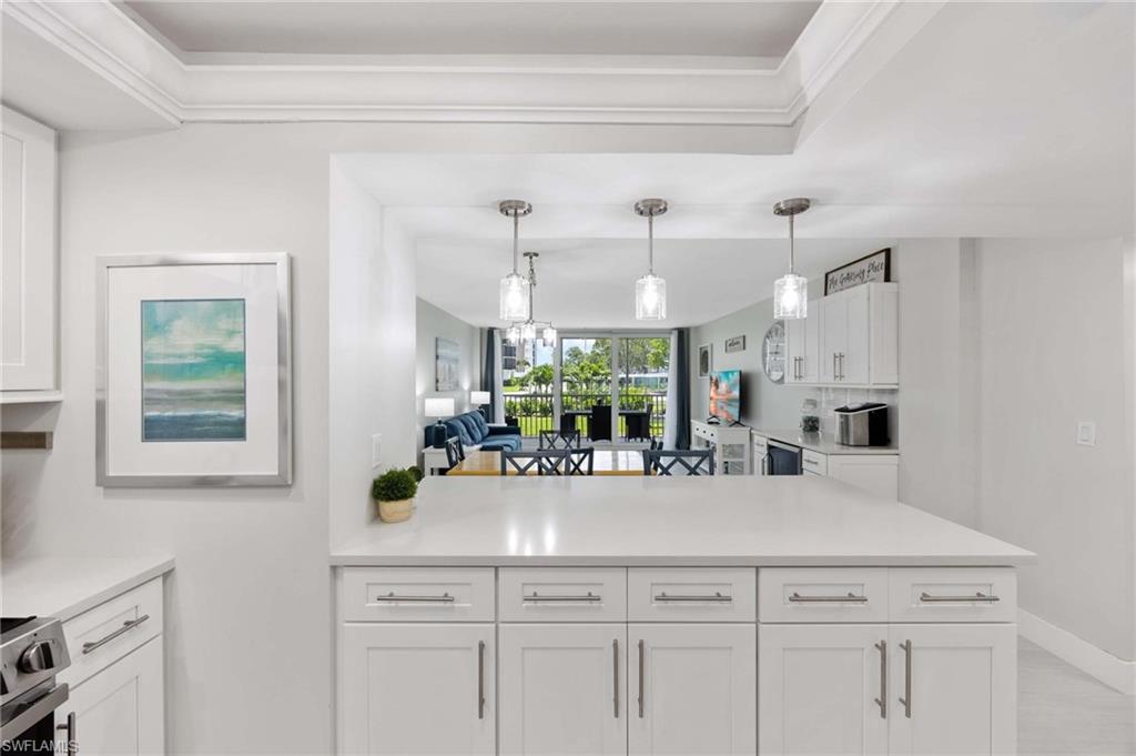 5 Bluebill Avenue, Unit 108 Naples, FL 34108 - Photo 7 of 49 Kitchen featuring stainless steel range with electric cooktop, white cabinets, light countertops, decorative light fixtures, and crown molding