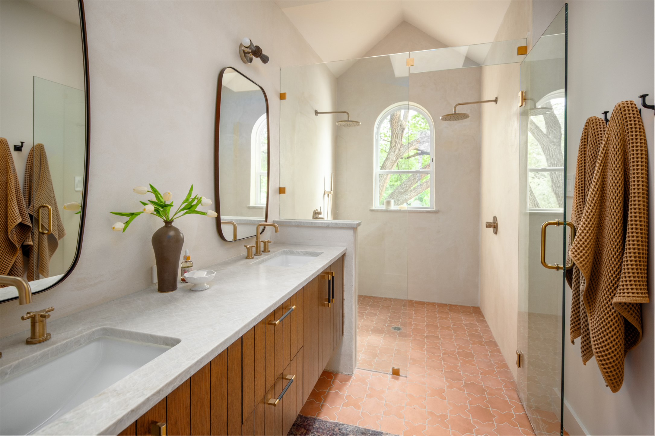 4713 Bolm Road Austin, TX 78702 - Photo 28 of 40 Spacious bathroom featuring a dual vanity with wood cabinetry and undermount sinks, a large glass-enclosed shower with dual shower heads, a vaulted ceiling, and arched windows