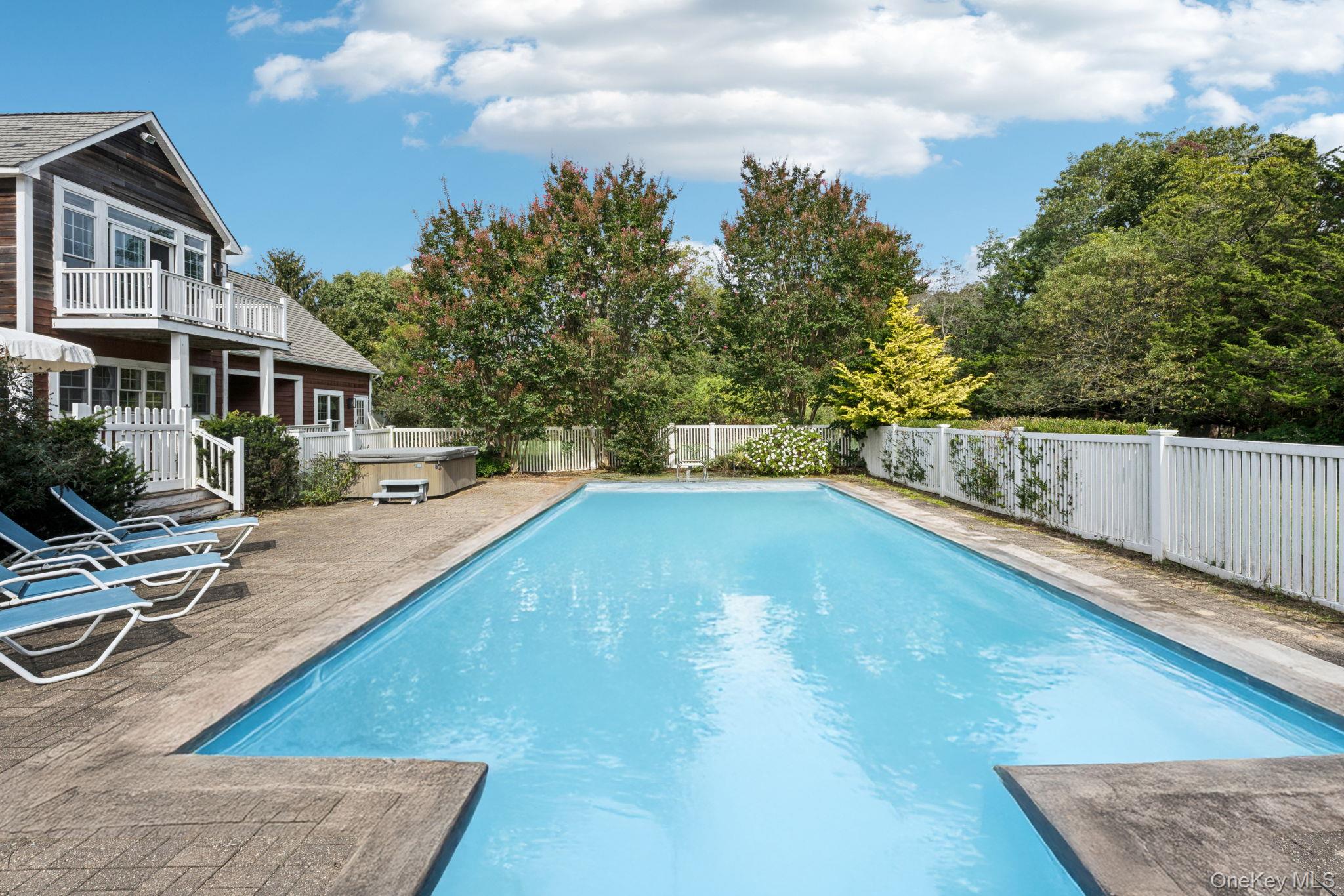 12 Laila Lane Remsenburg, NY 11960 - Photo 37 of 50 A captivating view reveals the swimming pool, sunlit patio, and spa, all surrounded by a private fenced backyard and complemented by a balcony that overlooks this serene outdoor haven.