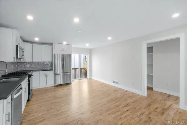 a view of kitchen with stainless steel appliances granite countertop a stove top oven a refrigerator and white cabinets with wooden floor
