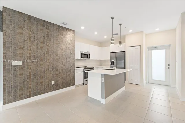 a large kitchen with a refrigerator a sink dishwasher a stove and white cabinets with wooden floor