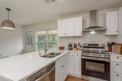 a kitchen with stainless steel appliances sink a stove and white cabinets