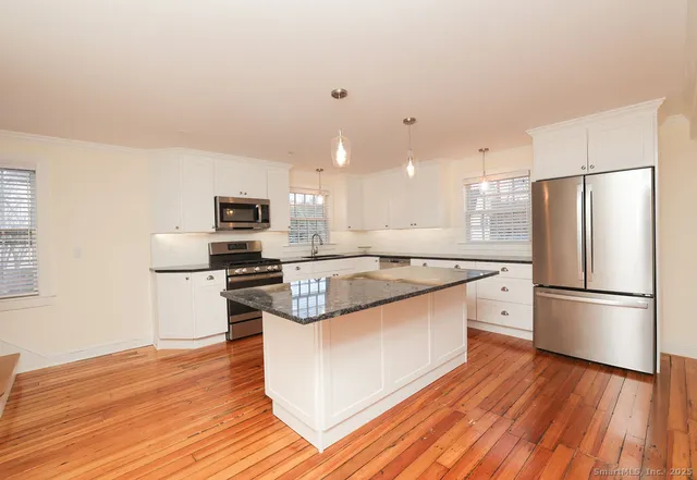 a kitchen with stainless steel appliances granite countertop a refrigerator a stove top oven a sink dishwasher and a refrigerator with wooden floor
