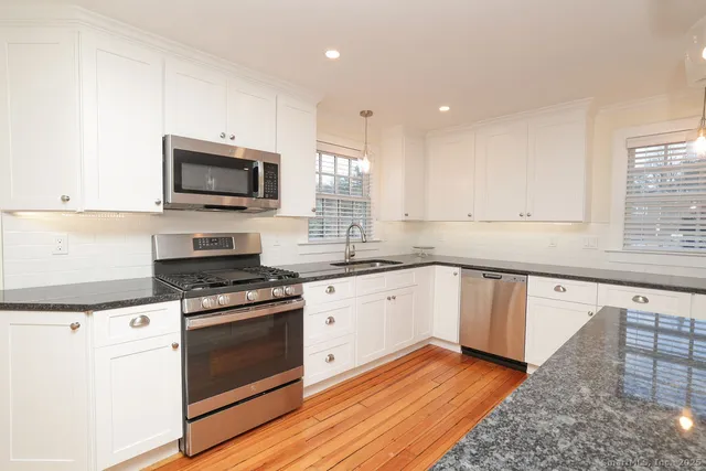 a kitchen with granite countertop a stove top oven a sink dishwasher and white cabinets with wooden floor