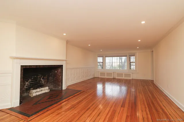 a view of an empty room with wooden floor fireplace and a window