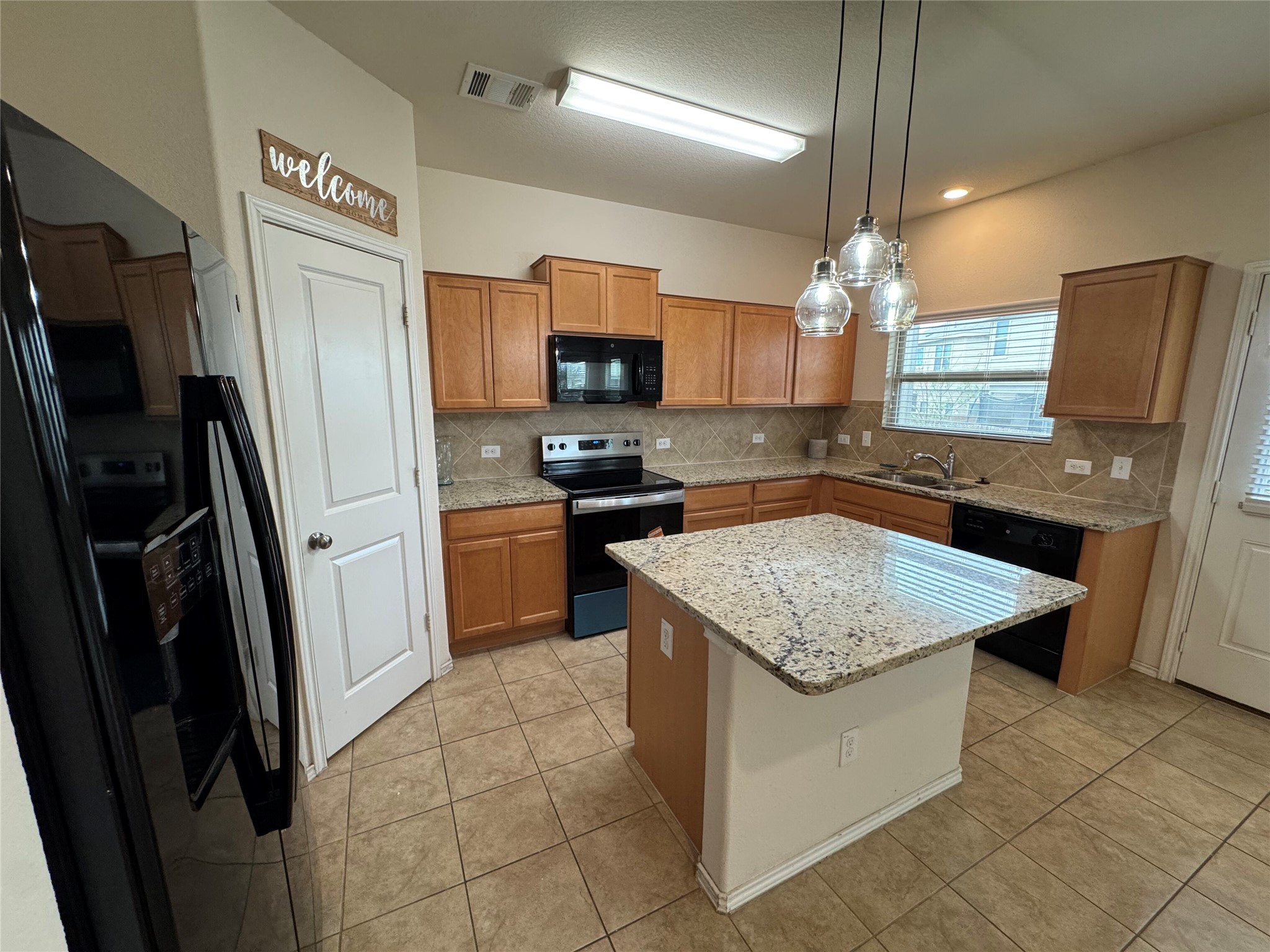 1108 Jackson Lane, Unit 5B Jarrell, TX 76537 - Photo 27 of 29 Kitchen with black appliances, a kitchen island, wood finish cabinetry, light stone counters, and tasteful backsplash