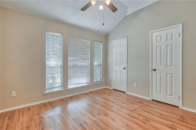 an empty room with wooden floor chandelier fan and windows